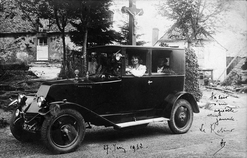 Femme au volant d'une automobile (veitura) devant une croix (crotz) en pierre, en Aubrac (secteur de Laguiole), 27 juin 1932