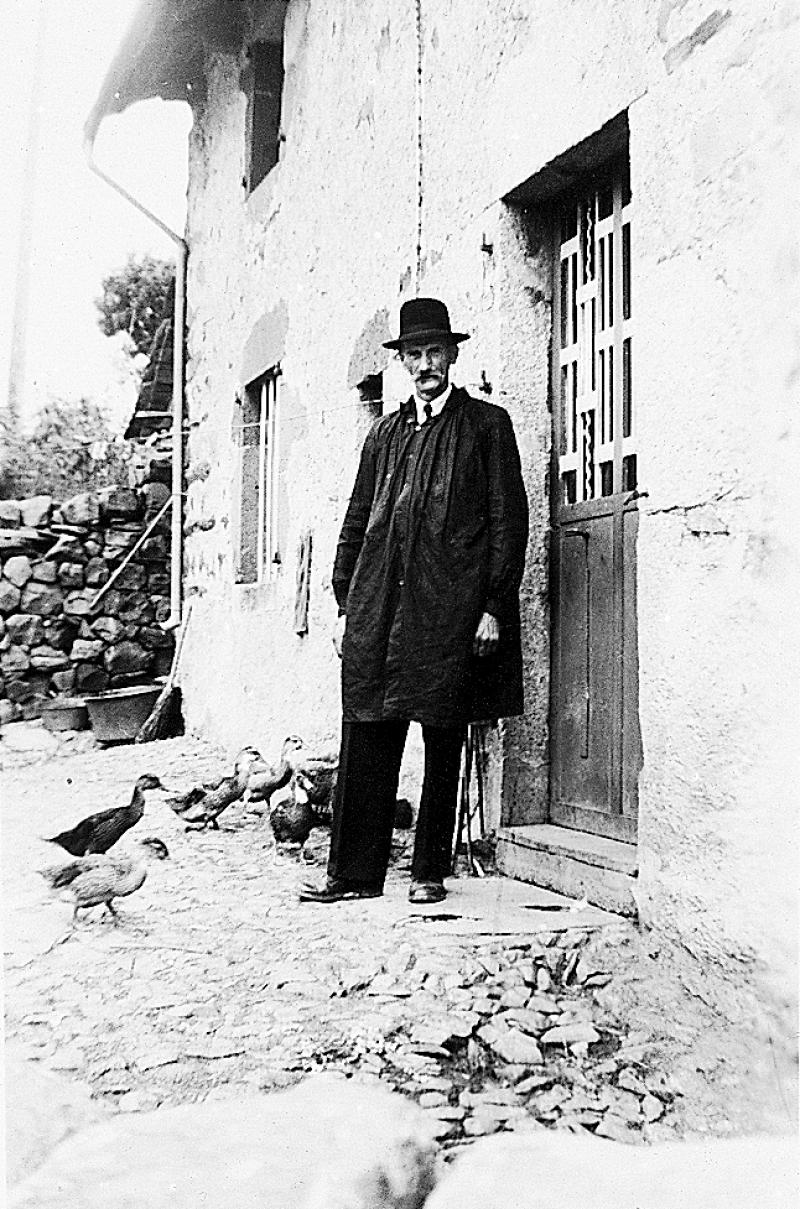 Homme en blouse devant porte d'entrée de maison, à La Bessière