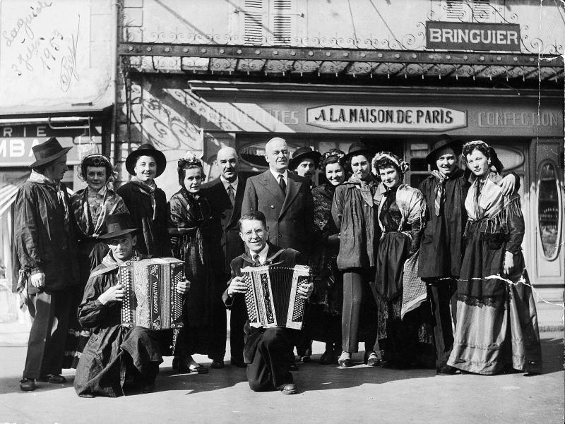 Deux accordéonistes (acordeonistas), élus (elegits) et groupe folklorique costumé devant une devanture (veirina) de magasin, 3 juin 1953