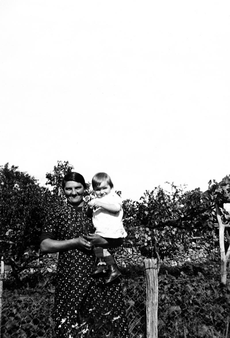  Femme avec fillette dans les bras dans un jardin (òrt)