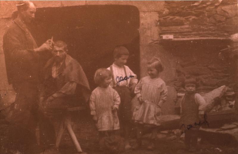  Coiffeur (perruquièr) au travail devant une porte d'étable et enfants, à Aunac, 1929