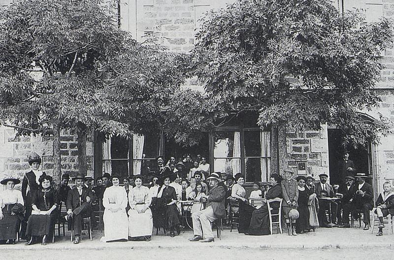 Serveuses, clientèle endimanchée attablée à la terrasse d'un café et joueur de cabrette (cabretaire), à Aubrac, 1906
