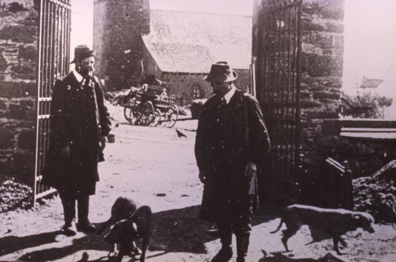 Deux chasseurs (caçaires) et deux chiens (cans) devant portail (portal) en fer forgé, à Bonnefon, vers 1919