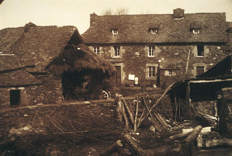 Homme fendant du bois (lenha) dans une cour de maison (ostal), à Aunac, 1927