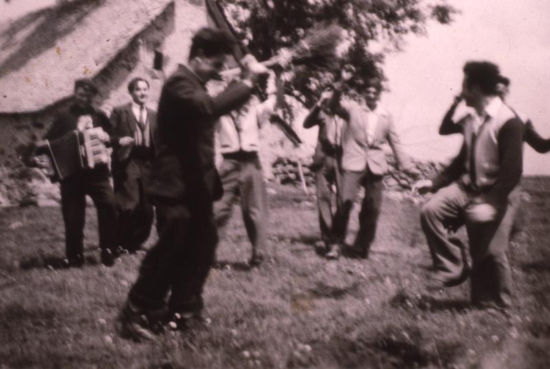 Accordéoniste (acordeonista), danseurs de bourrée (dançaires de borrèia) et homme avec un balai (balag, balaja) devant un buron (masuc), sur une Montagne (montanha) de Laguiole