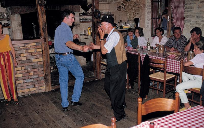  Deux hommes dansant la bourrée (borrèia), dont un jouant de l'harmonica, devant clients attablés dans une auberge (aubèrja), à Boulouis, 2007
