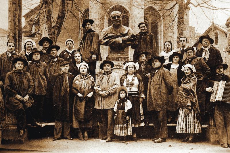  Membres (grelhons) costumés du Grelh roergàs avec accordéoniste (acordeonista) devant le monument de l'abbé Justin Bessou, entre les allées de la Résistance et le quai de la Sénéchaussée