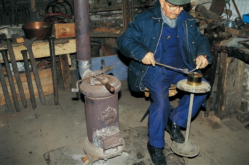Homme dans son atelier soudant à l'étain (estam) une boîte de conserve, rue  de l'étameur (estamaire), janvier 1995 | Occitan Aveyron