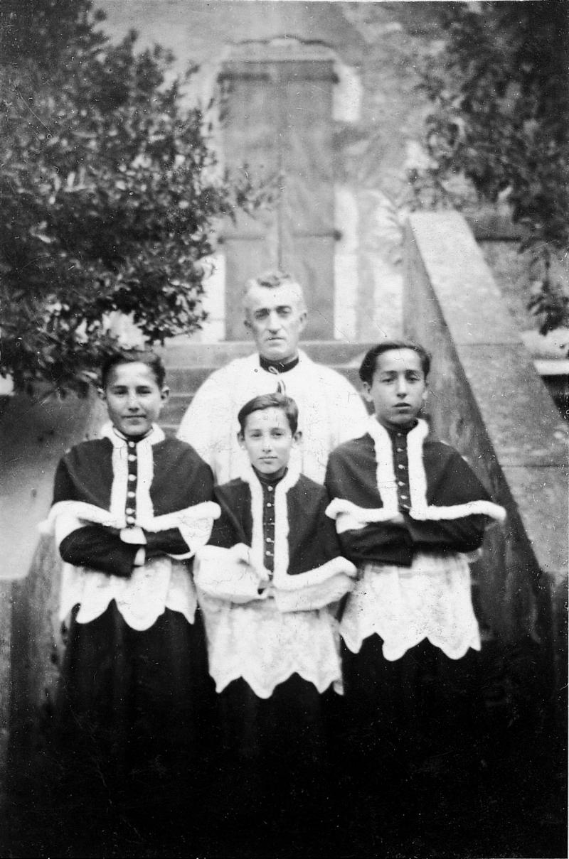 Trois enfants de chœur (clergues) avec un curé (curat) en bas d'un escalier