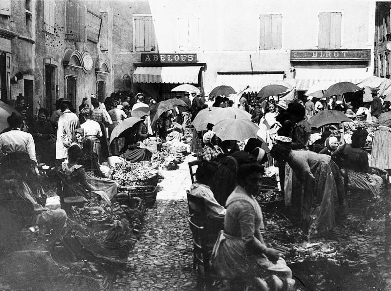 Etals de marchandes (merchandas) de légumes et clientes sur une place un jour de foire (fièira) ou de marché (mercat)