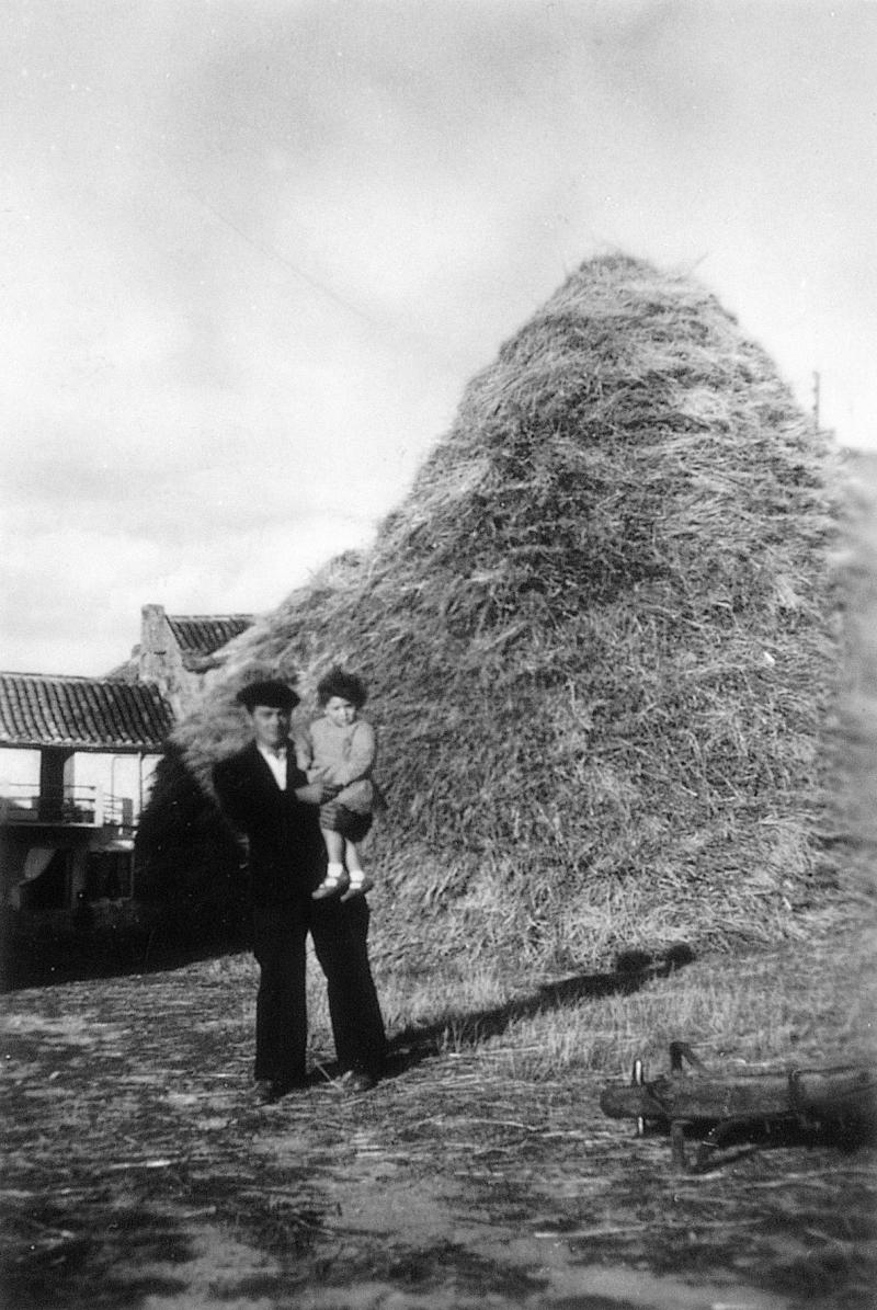  Homme avec un garçon dans les bras devant un gerbier (plonjon), à Alcapiès, 1960