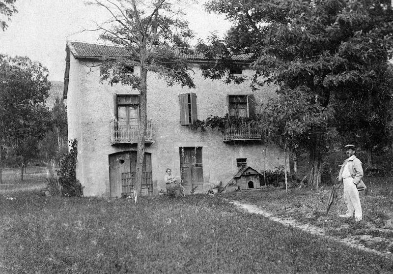 Femme assise et homme devant une maison (ostal), à Cantillergues