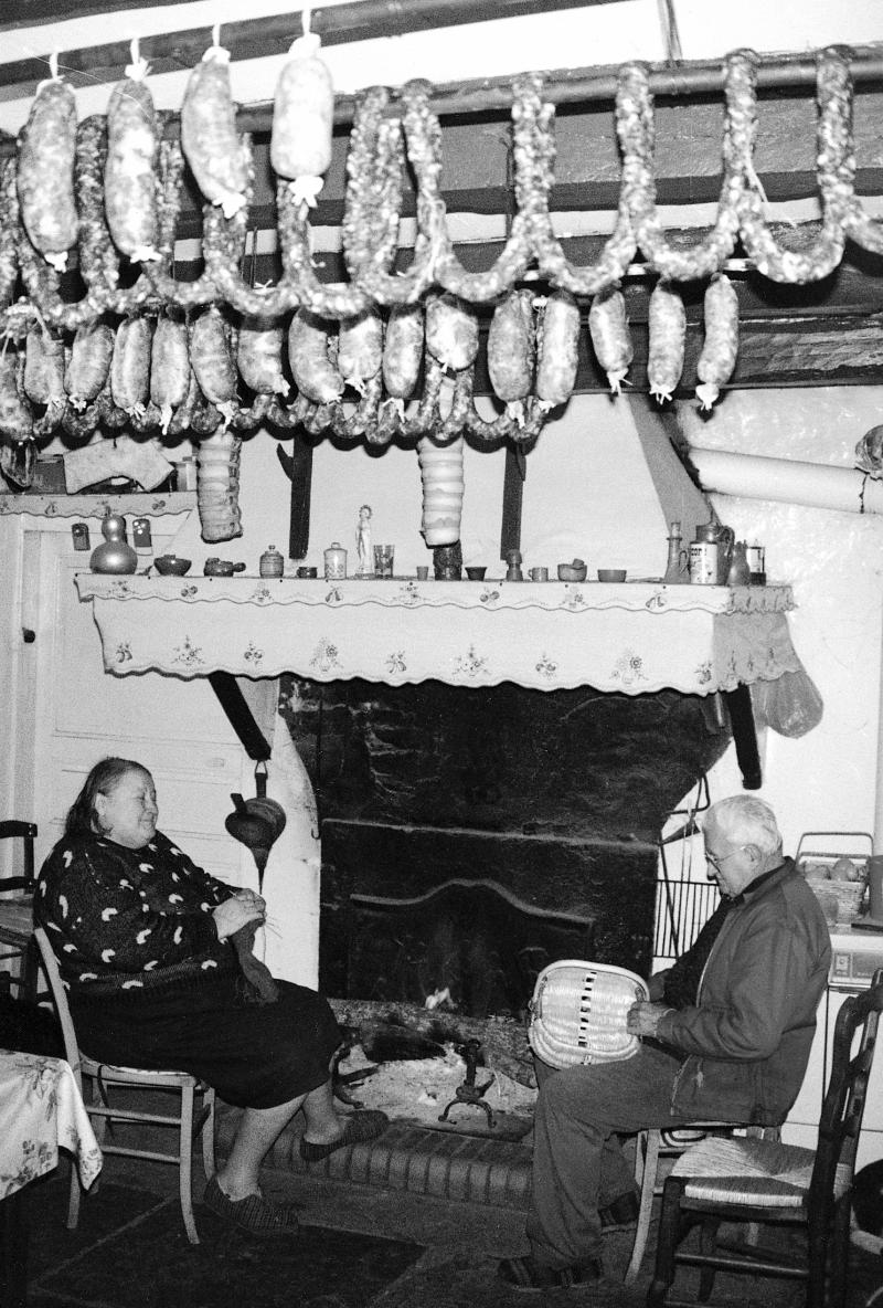 Femme tricotant et homme confectionnant un panier (panièr) au coin du feu (canton), saucisse (salsissa) et saucissons (salsissons) supendus au plafond, à Ségonzac, 1995
