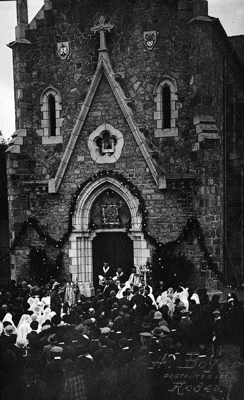 ​Foule, jeunes filles voilées, évêque (evesque) et curés (curats) rassemblés devant la porte d'entrée de l'église (glèisa) pour son inauguration