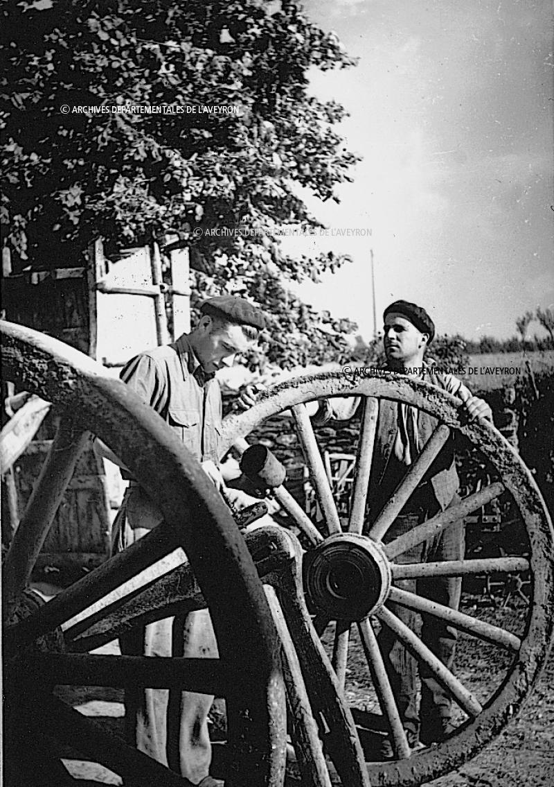 Hommes graissant (ónger) l'essieu (ais) d'une roue de char (ròda de carrii), à Puech Amans, 1945