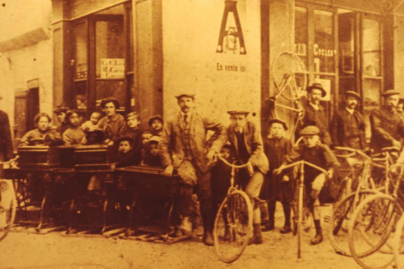 Couturières (cordurièiras, cosièiras) avec machines à coudre, marchand de bicyclettes devant leur magasin et enfants avec bicyclettes