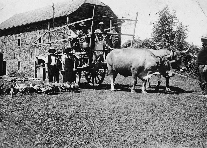 Famille à côté et sur un char-cage ou à claies (carri de castre o de cleda) et paire de bovidés (parelh) devant une grange (fenial, granja), 1940