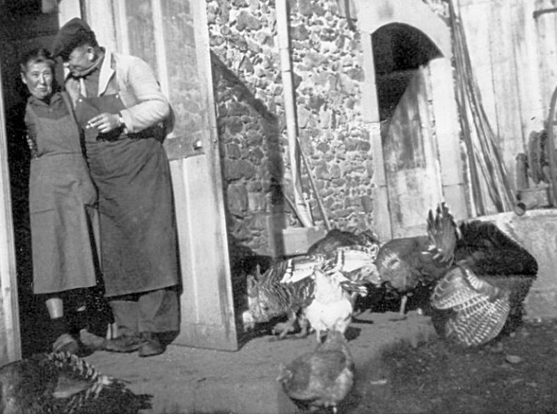 Femme et laitier (lachièr) sur le pas de porte d'une maison (ostal),  poule (galina, pola) et dindons (piòts), à Grascazes