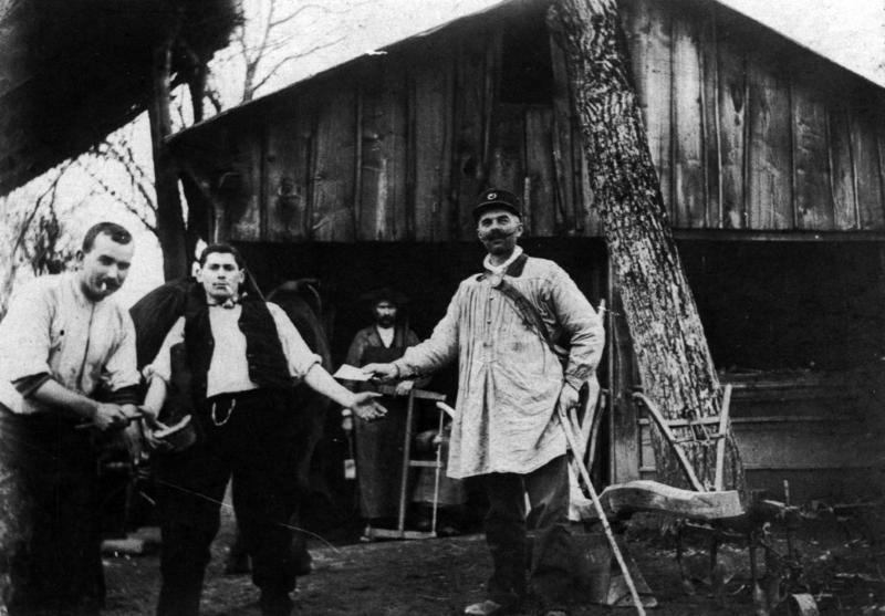 Ferrage d'un équidé et facteur (portur) de Sauveterre de Rouergue distribuant une lettre devant un hangar en bois (cabanat), à Cabanès, 1920