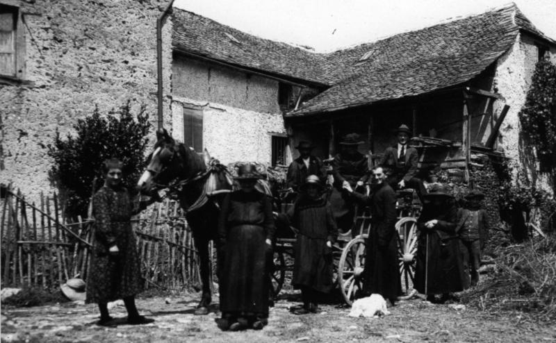 Famille avec curé (curat) devant et sur un break attelé à un équidé dans la cour d'une maison (ostal) avec balcon couvert (balet), au Frayssinet