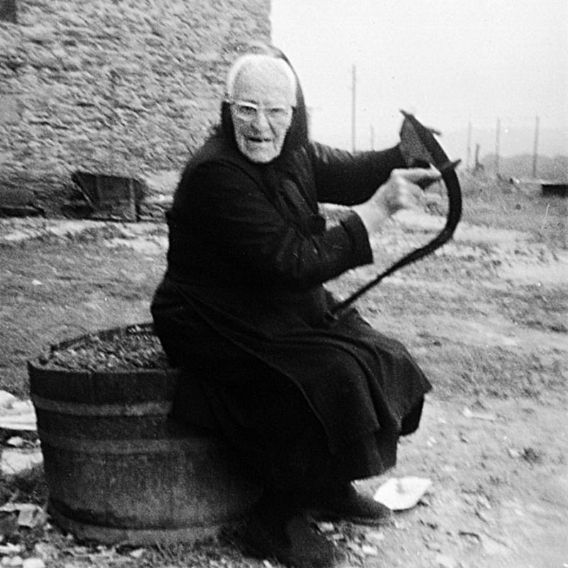 Femme assise sur un baquet (barquet) aiguisant une faucille (volam) avec une pierre à aiguiser (cot), aux Agades, 1963