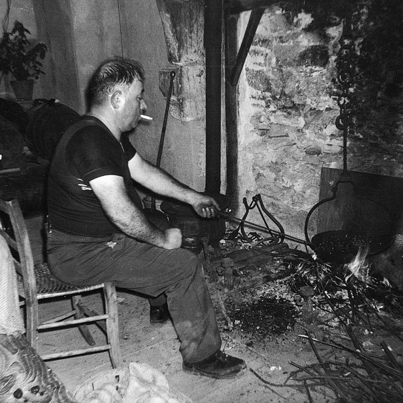 Homme faisant griller des châtaignes (castanhas) assis au coin du feu (canton), novembre 1964