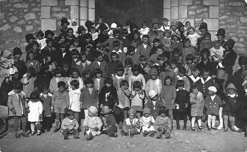 Enfants (dròlles, enfants) et paroissiennes (parroquianas) devant la porte de l'église (glèisa) pour une messe pour les enfants (messa pels dròlles), 1930