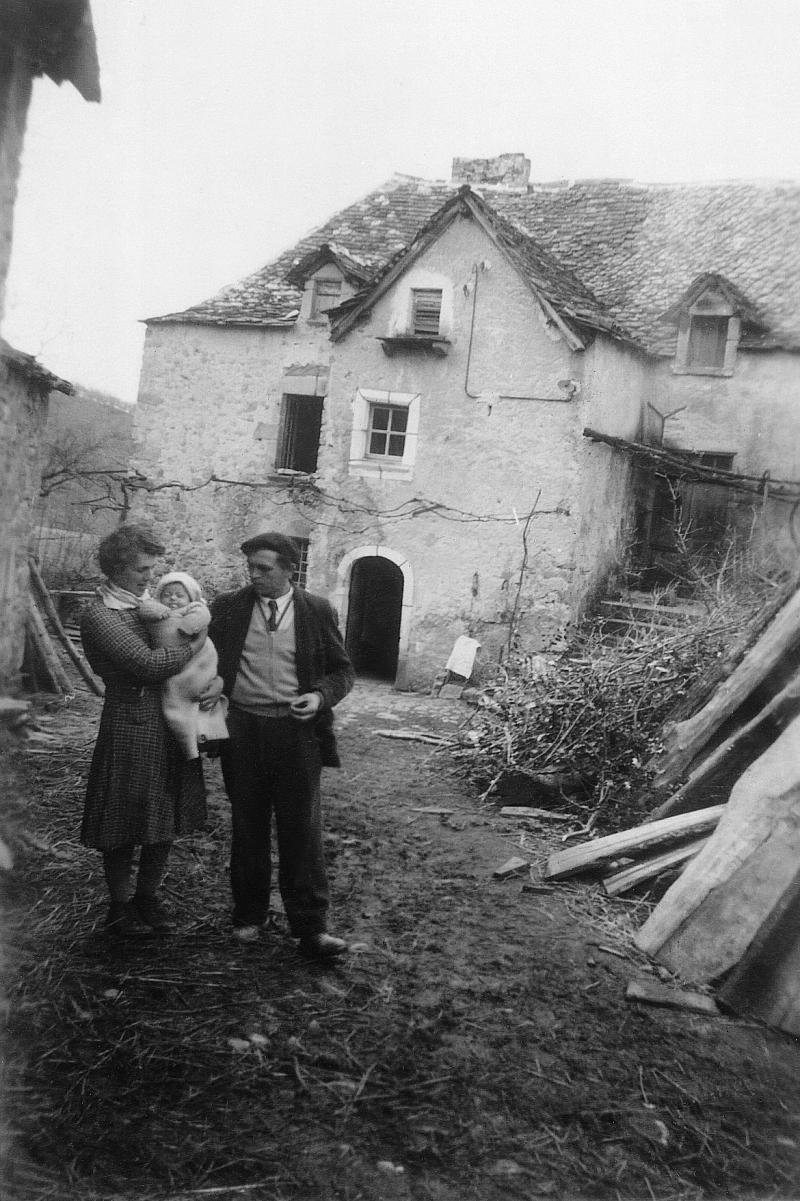Femme avec un nourrisson (nene, nenon) dans les bras et homme devant une maison (ostal) pour un baptême (batejalhas), au Rieu, 1956