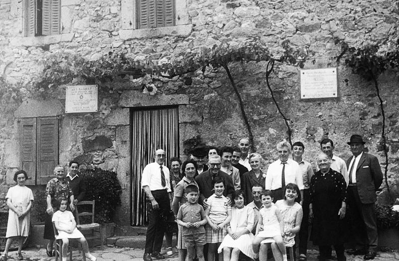 Famille devant la maison natale (ostal naissedor) de l'abbé Justin Bessou, plaques commémoratives écrites en occitan, à Méjalanou