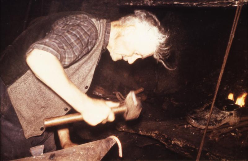 Homme dans une forge (farga) façonnant un morceau de fer sur une enclume (enclutge), au Pibol, 1968